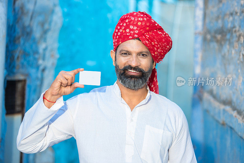 传统的印度年轻人展示空白的白色借记卡/信用卡模型，戴着红头巾、留着胡子的人拿着空的商业或电子卡进行支付，选择性聚焦。